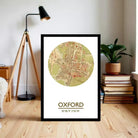 A framed map of Oxford, UK, with a lamp and books in the background.