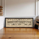 a large framed map of a city, with a detailed and intricate design, displayed on a wooden floor against a white wall.
