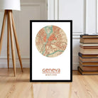 A framed map of Geneva, Switzerland, with the text " Geneva" and "46°N 6°E" printed on it, is displayed on a wooden floor next to a stack of books.