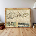 a large, old map of a region, possibly a country or island, displayed on a wooden floor. The map appears to be framed and is surrounded by a few books and a lamp.