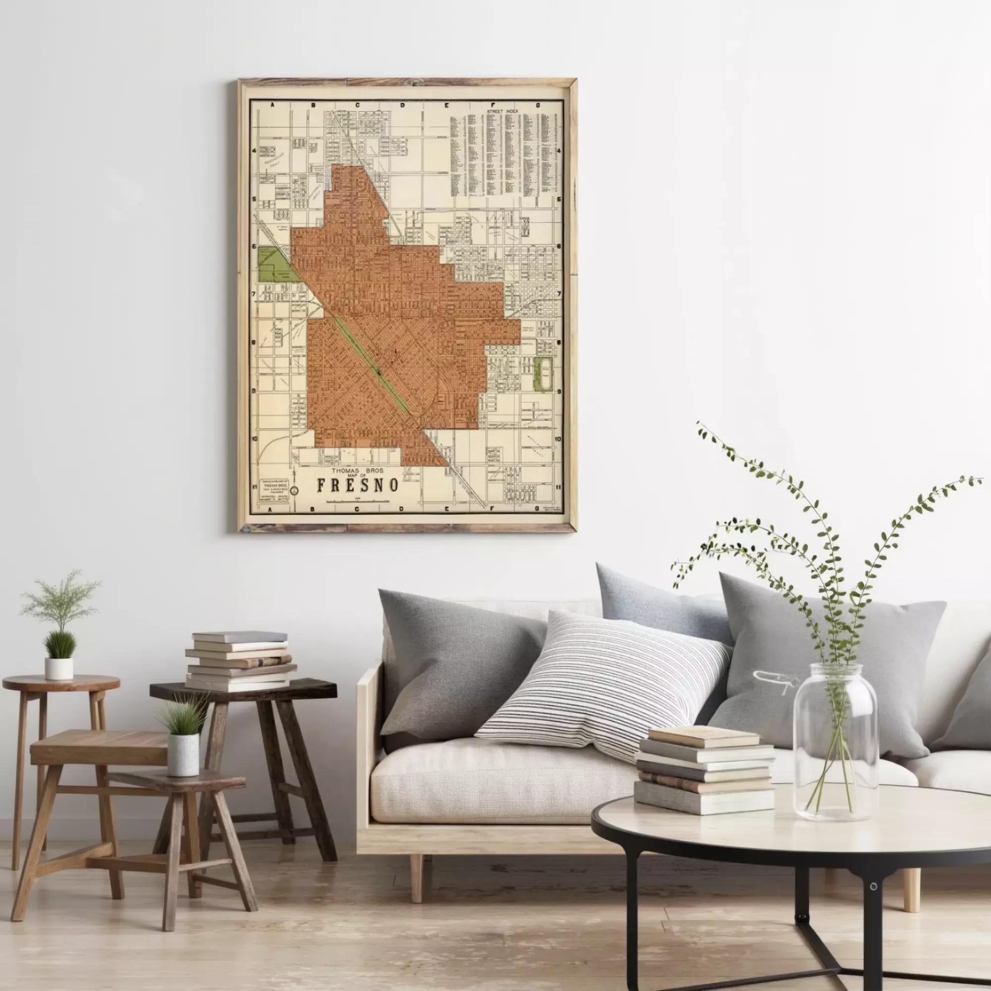 a living room with a framed map of Fresno hanging on the wall above a couch with pillows. The room has a wooden coffee table, a small side table, and a vase with greenery.
