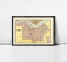 The image is a framed vintage map of a city, likely from the early 20th century, with a yellow and pink color scheme.