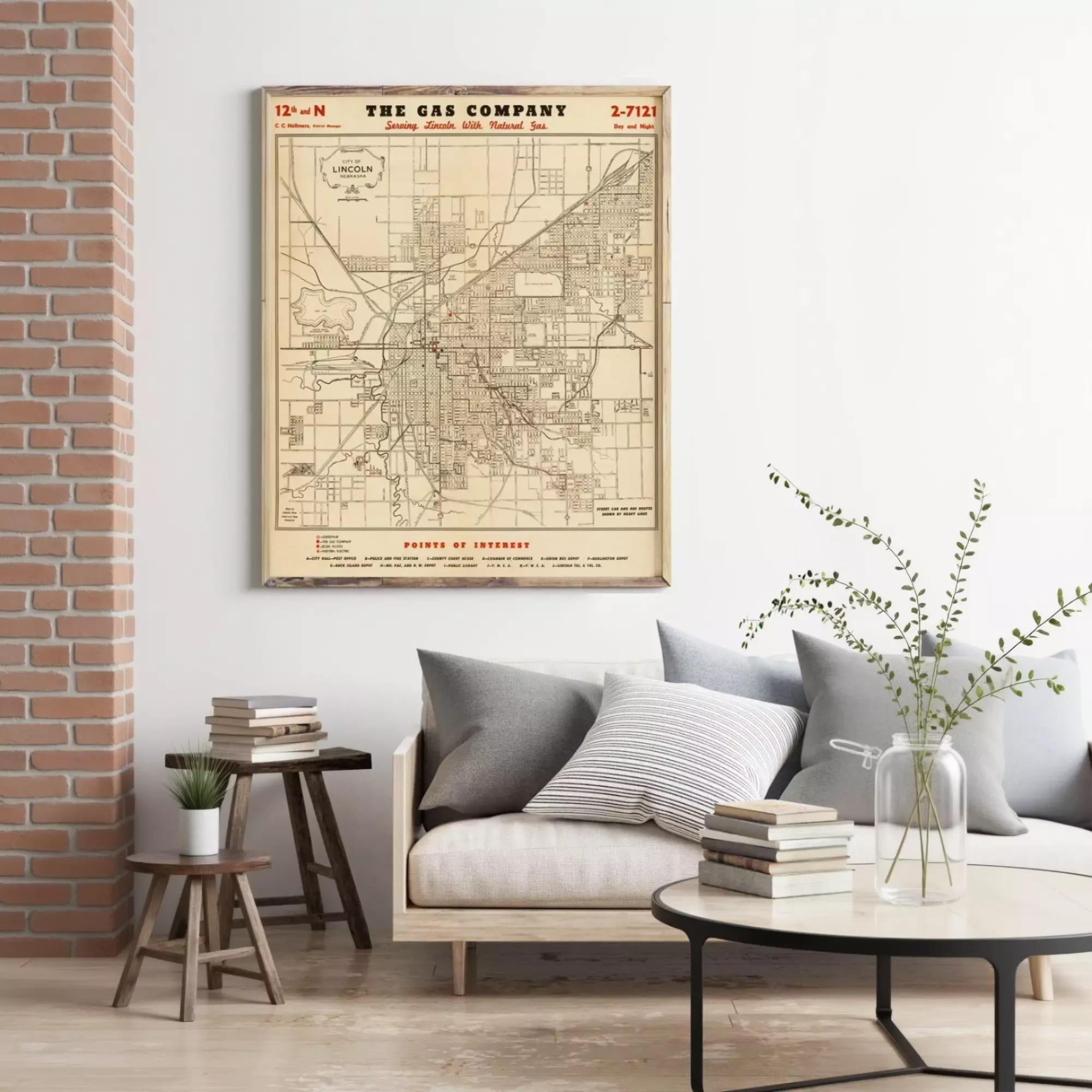 a living room with a large framed map of the Lincoln, Nebraska area hanging on the wall. The room has a couch, a coffee table, and some books and plants, creating a cozy and inviting atmosphere.