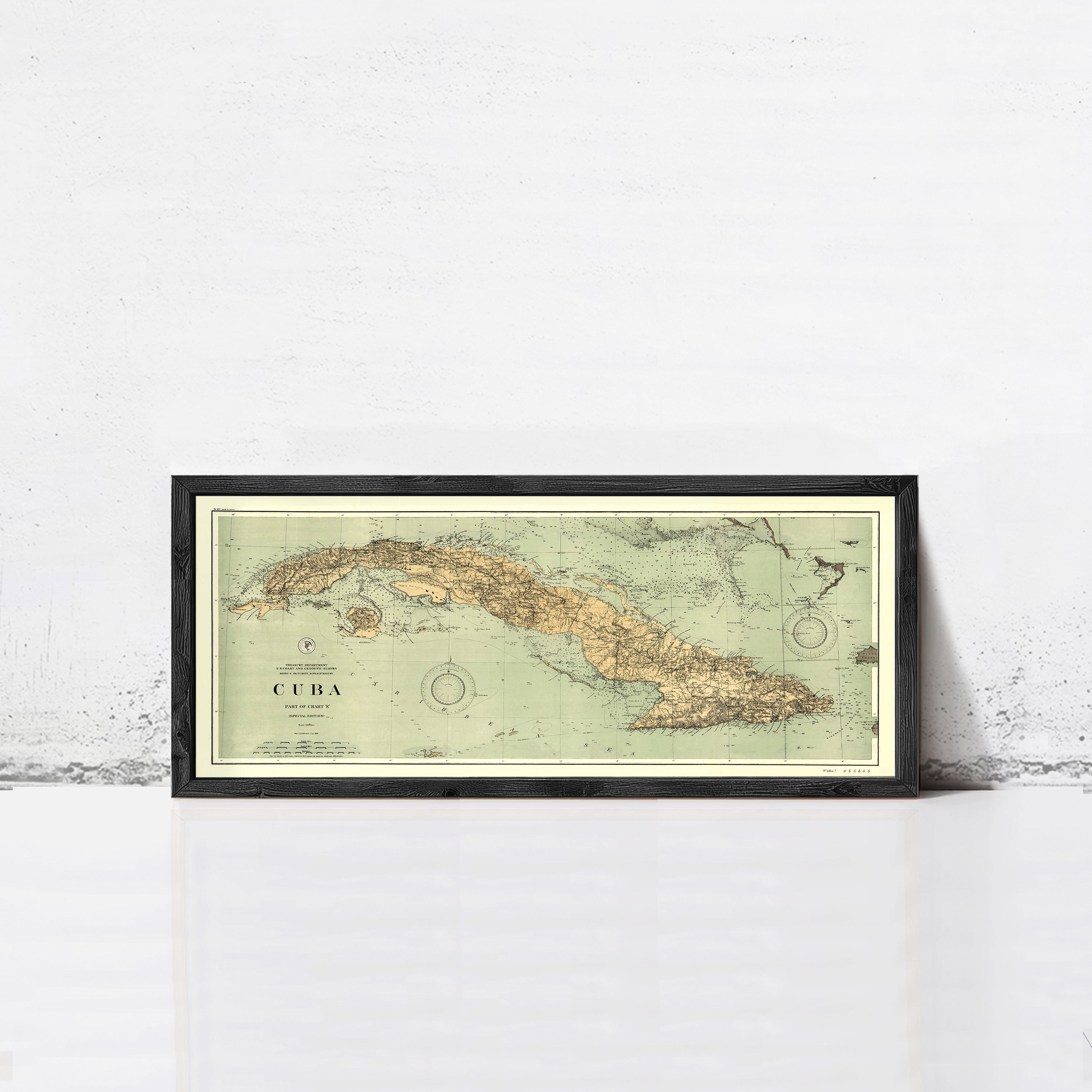 A framed vintage map of Cuba is displayed against a white wall.