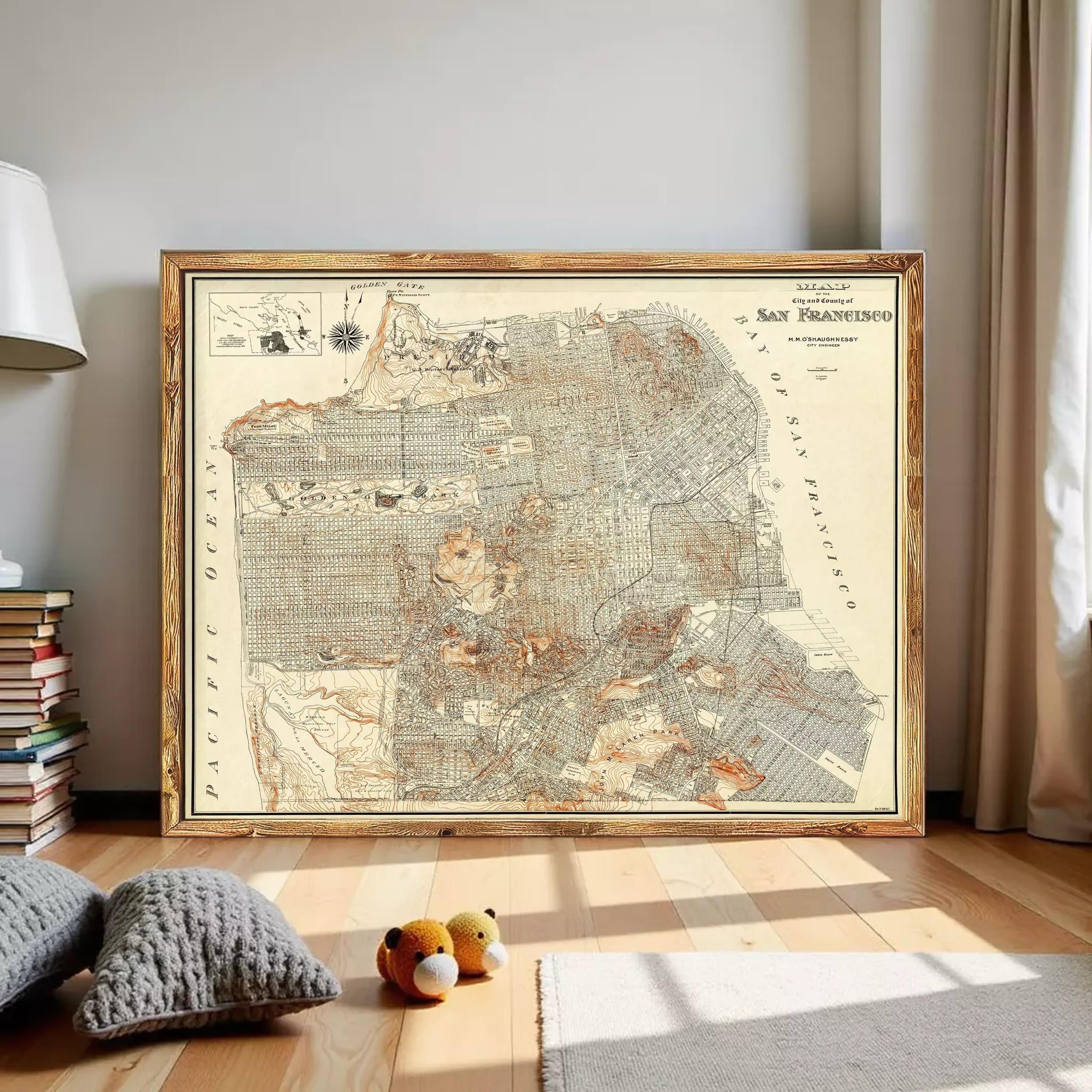 a large framed map of San Francisco, with a wooden frame and a vintage style. The map is displayed on a wall in a room with a wooden floor. There are also some stuffed animals, specifically two teddy bears, placed on the floor in front of the map.