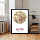 A framed map of Poznan, Poland, with the name "Poznan" printed on it, is displayed on a wooden floor next to a stack of books and a lamp.