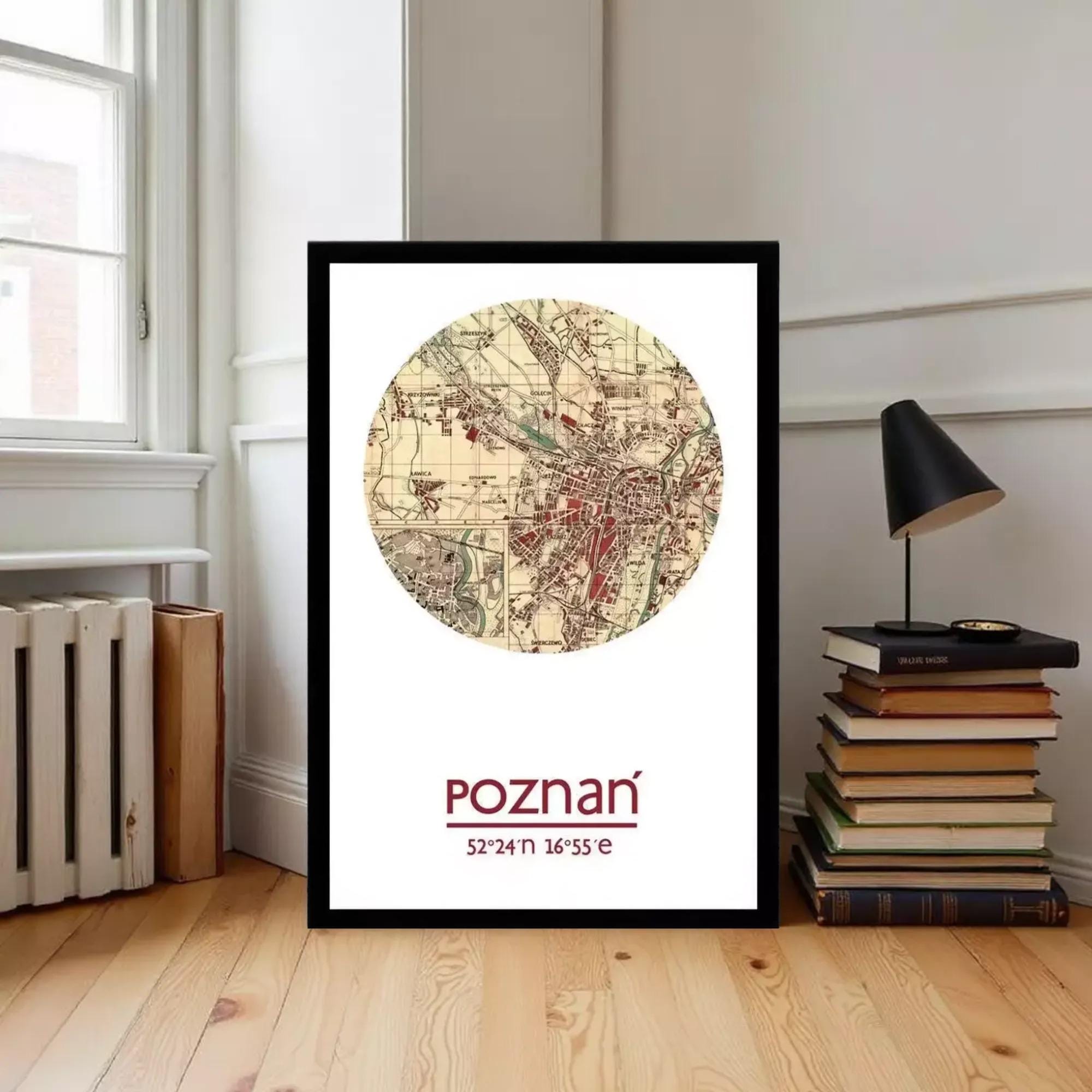 A framed map of Poznan, Poland, with the name "Poznan" printed on it, is displayed on a wooden floor next to a stack of books and a lamp.