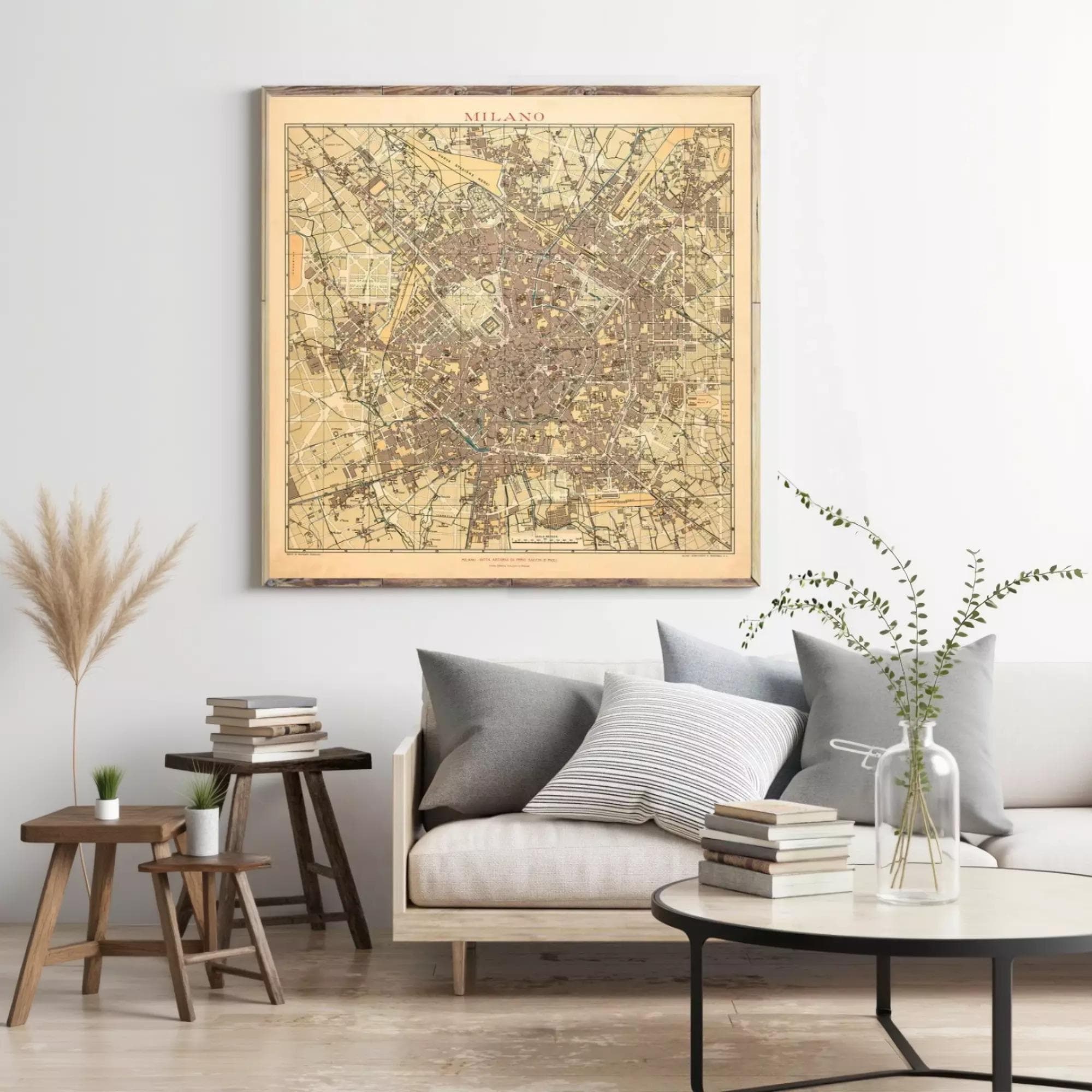 a living room with a large framed map of Milan hanging on the wall above a couch with pillows. There are also some books and decorative items on the couch and table below the map.