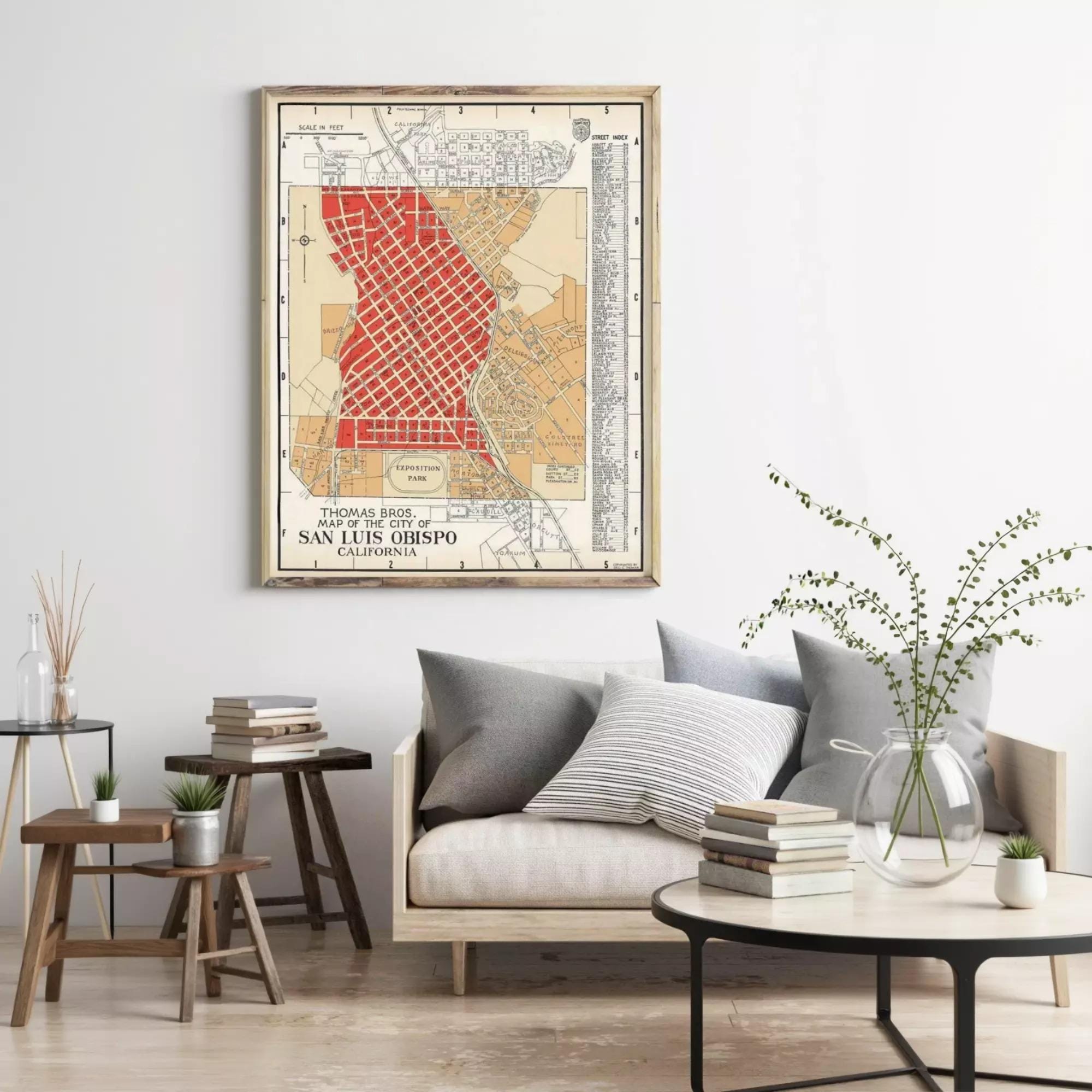 a living room with a framed vintage map of San Jose, California, hanging on the wall above a couch with pillows. The room also includes a coffee table with books and a vase of flowers, creating a cozy and inviting atmosphere.
