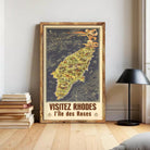 The image is a framed poster depicting a map of Rhodes, Greece, with the text "VISITÉZ RHODES I l'ile des Roses" (Visiting Rhodes, the island of roses) at the bottom.