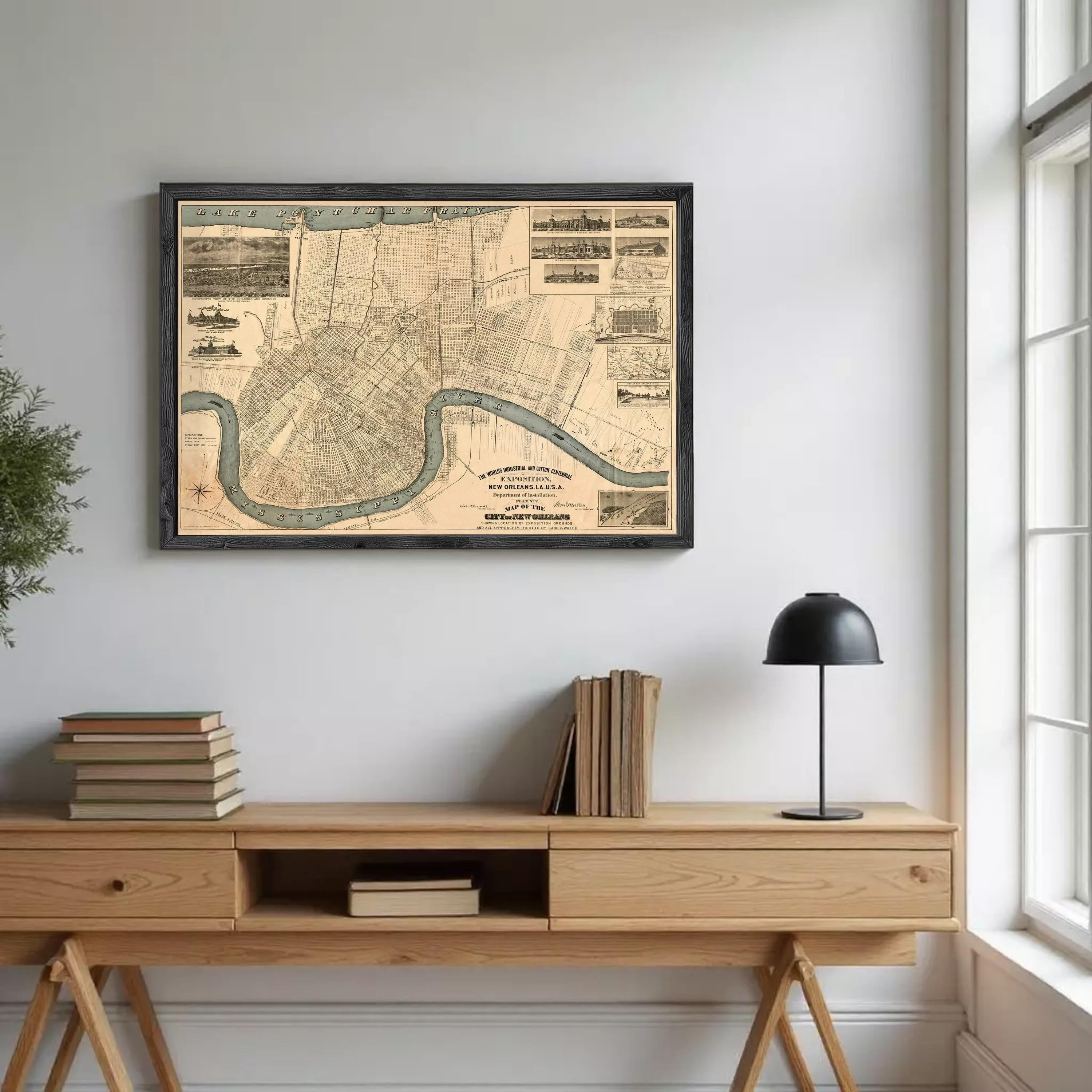 a wooden desk with a lamp, a stack of books, and a framed map of New Orleans hanging on the wall above it.