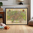 A framed map of Cambridge, England, displayed on a wooden floor in a room with a lamp and books.