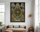 The image is a framed painting depicting a mandala with various figures and symbols surrounding it.