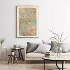 a cozy living room with a large framed map of New York City hanging on the wall above a gray sofa with striped pillows. The room also features a coffee table with a vase of greenery, a stack of books, and a small side table with a plant.