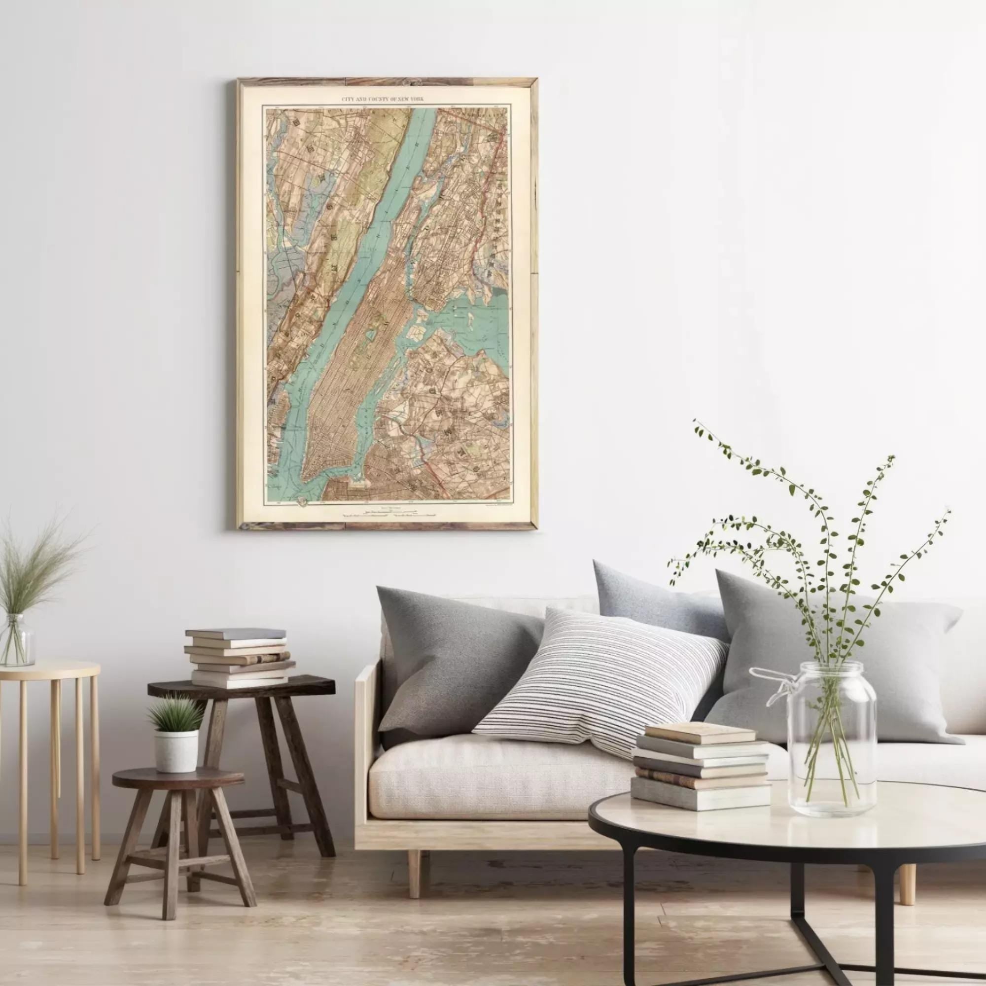 a cozy living room with a large framed map of New York City hanging on the wall above a gray sofa with striped pillows. The room also features a coffee table with a vase of greenery, a stack of books, and a small side table with a plant.
