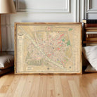 The image is a framed vintage map of a city, likely from the 19th century, displayed on a white wall.