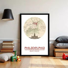 A framed map of Philadelphia, with a vintage-style illustration of the city's landmarks, is displayed on a wall in a room with a lamp and children's toys.