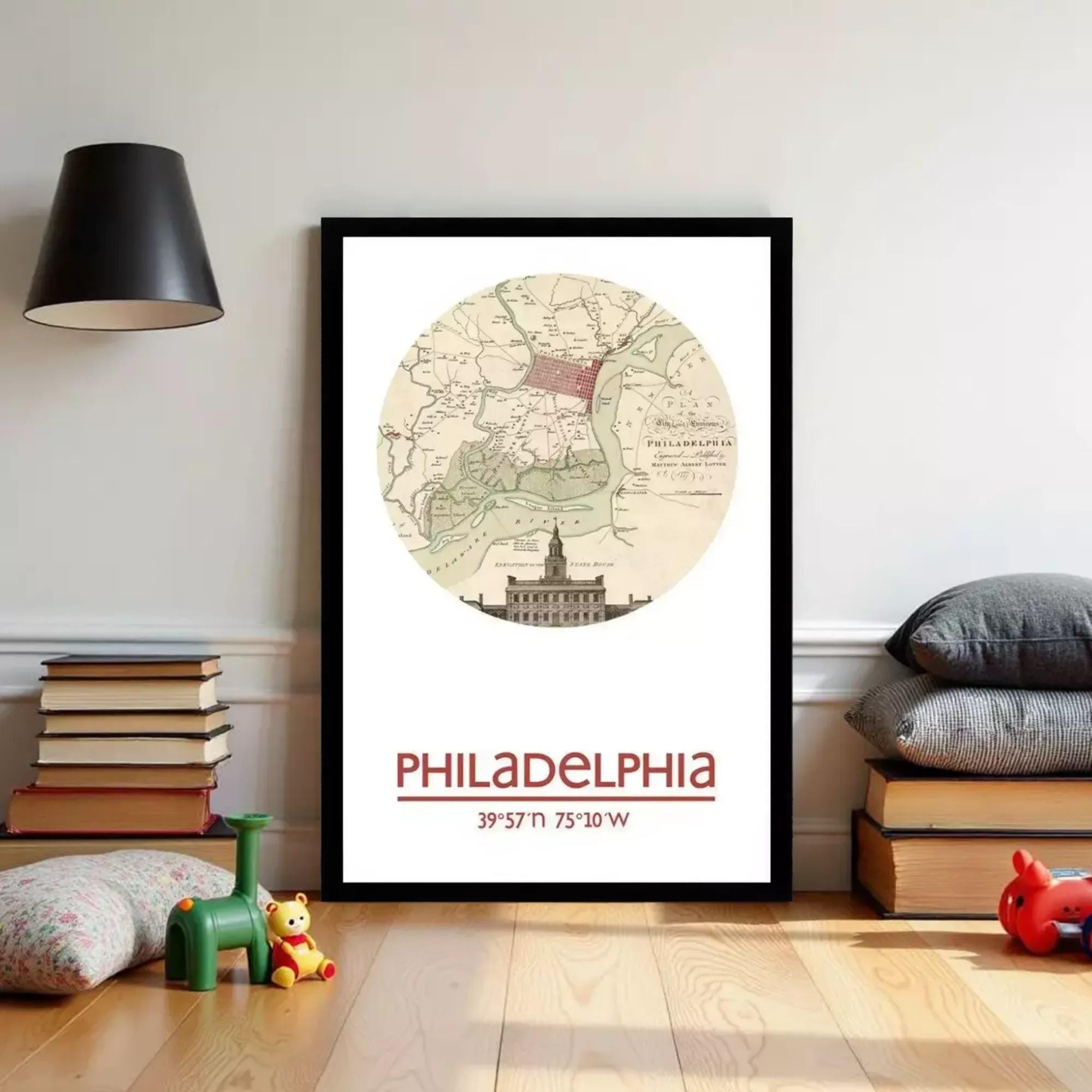 A framed map of Philadelphia, with a vintage-style illustration of the city's landmarks, is displayed on a wall in a room with a lamp and children's toys.