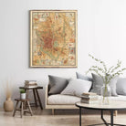 a living room with a large framed map hanging on the wall above a couch with pillows. There are also some books and a vase with flowers on the couch, creating a cozy and inviting atmosphere.