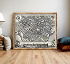 The image is a framed vintage map of a city, depicting a detailed layout of streets, buildings, and other urban features.