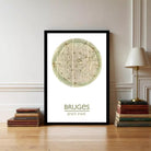 A framed poster of a map of Brussels, Belgium, displayed on a wall next to a stack of books and a lamp.