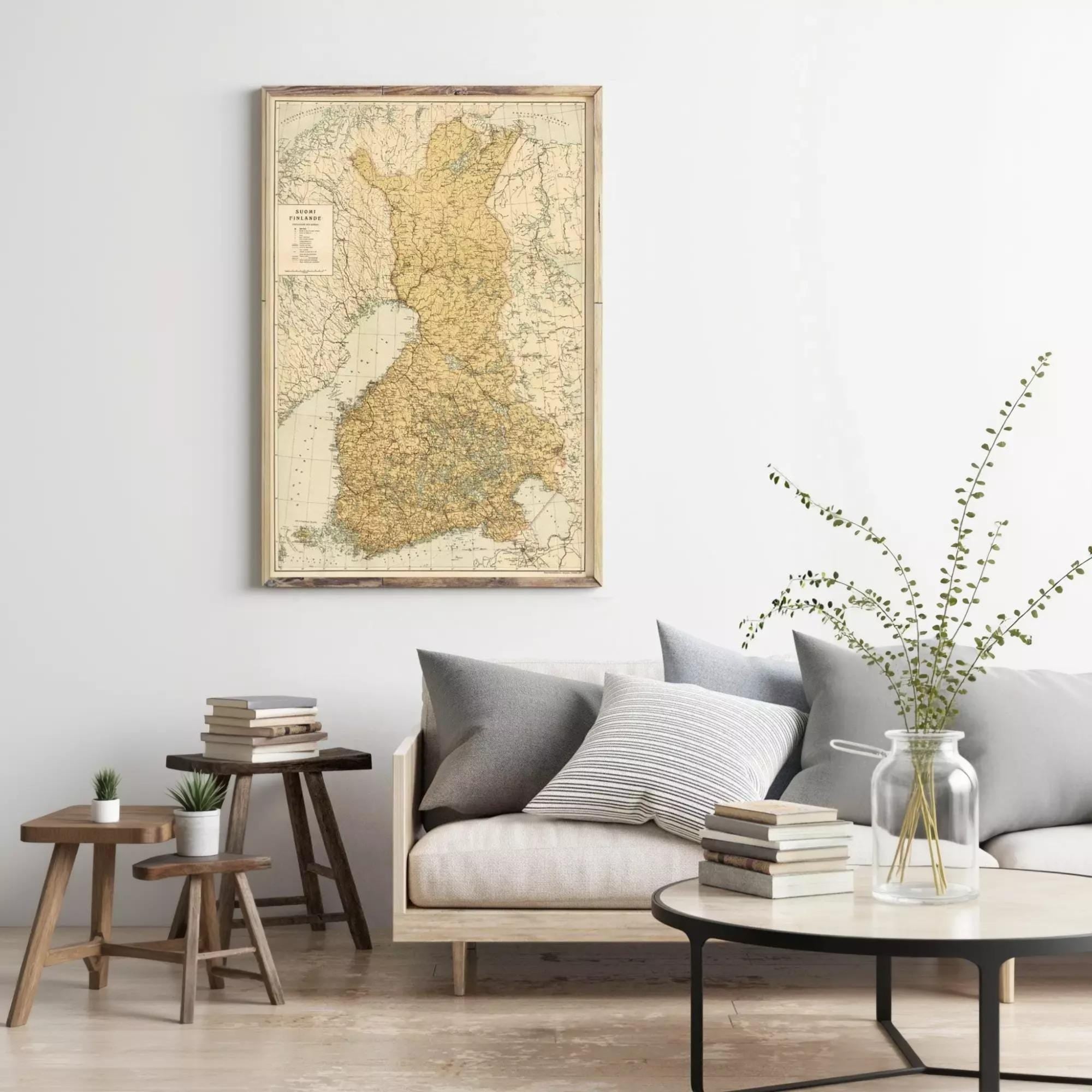 a living room with a large map of Finland hanging on the wall above a gray sofa with striped pillows. The room also includes a coffee table with a vase of greenery, a stack of books, and a small side table with a plant.