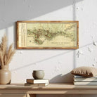 a framed map of Monaco hanging on a wall above a wooden shelf with books and a vase.
