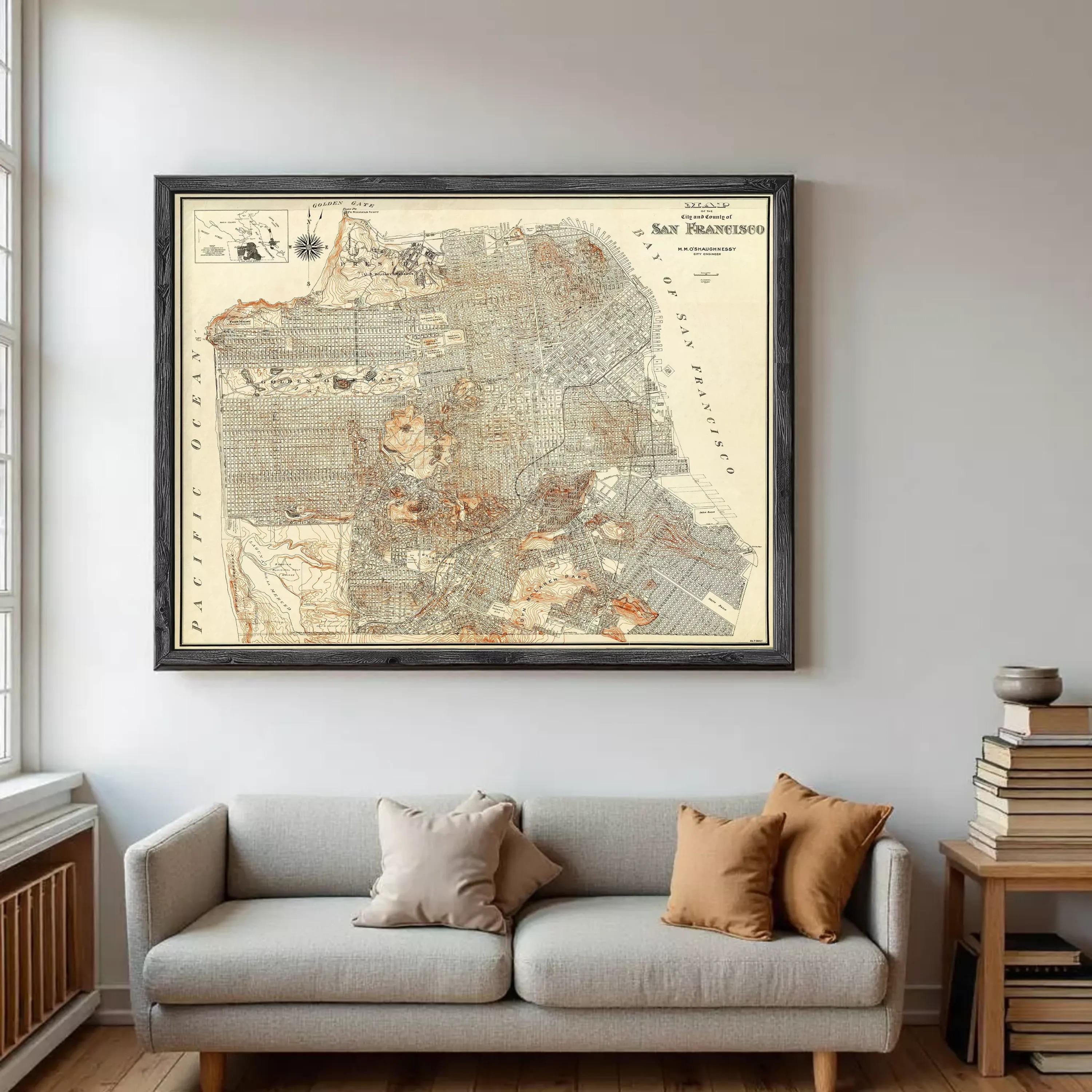 a large framed map of San Francisco hanging on a wall above a gray sofa with two pillows.