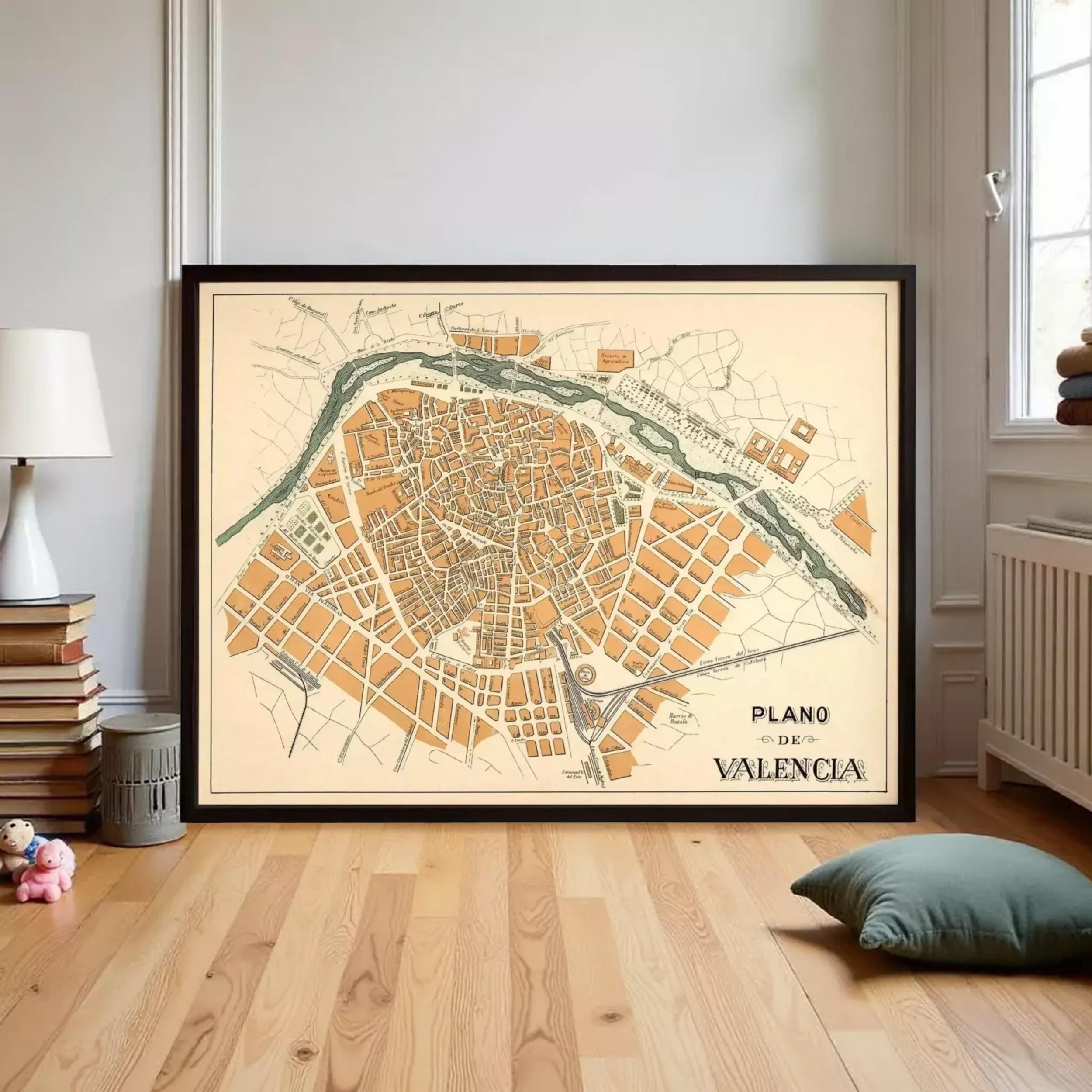 A framed map of the city of Valencias, Spain, displayed on a wooden floor in a room with a lamp and bookshelf.
