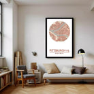 a living room with a large framed map of Pittsburgh, Pennsylvania, hanging on the wall. The map is circular and has a map-like design. The room is furnished with a couch, a chair, and a bookshelf. There are also some books and a lamp in the room.
