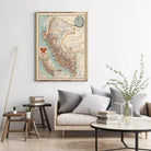 a living room with a large framed map of South America hanging on the wall above a couch with pillows. There are also some books and a vase with greenery on the coffee table in front of the couch.