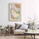 a living room with a large framed map of the Middle East hanging on the wall above a gray sofa with striped pillows. The room also includes a coffee table with a vase of greenery, a stack of books, and a small side table with a plant.