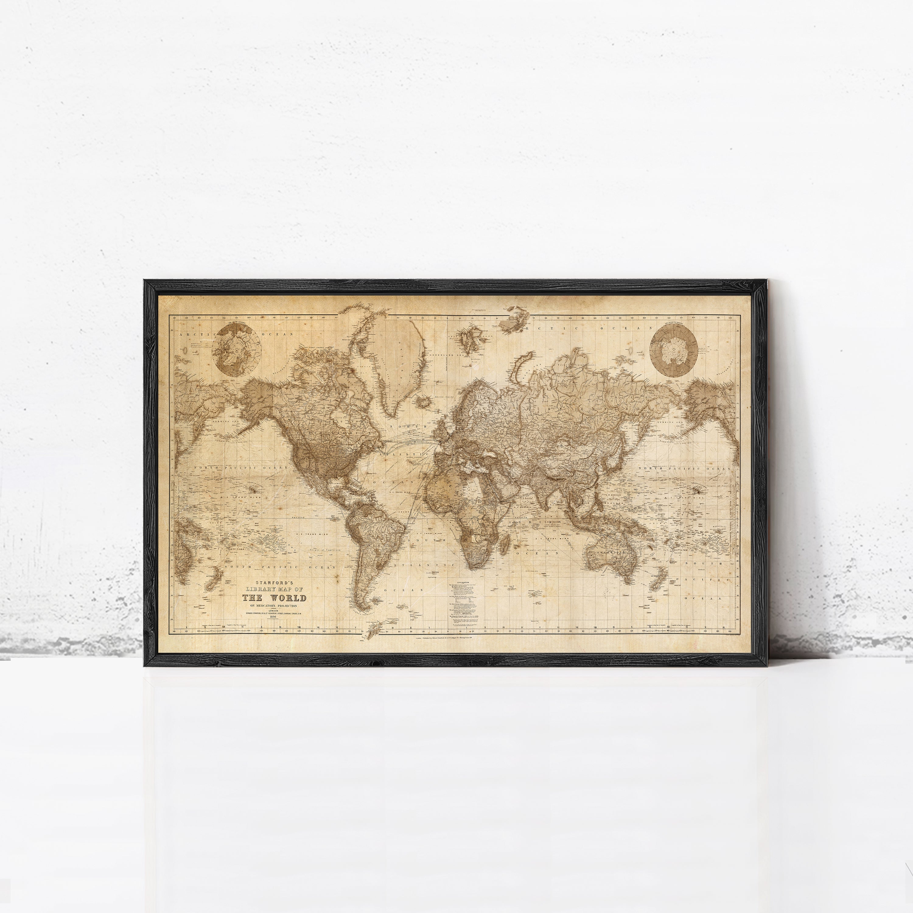 The image is a framed vintage world map with a black border, displayed on a white wall.
