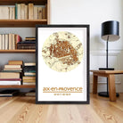 A framed map of Aix-en-Provence, France, with the text "aix-en-Provence" and "43°N 05°E" printed on it, is displayed on a wooden floor in front of a bookshelf.