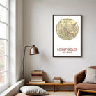 a framed map of Los Angeles, with the text "LOS ANGELES" and "34°37'11" 38°15'8" W" visible. The map is displayed on a wall in a living room setting, with a lamp, books, and a chair visible in the foreground.