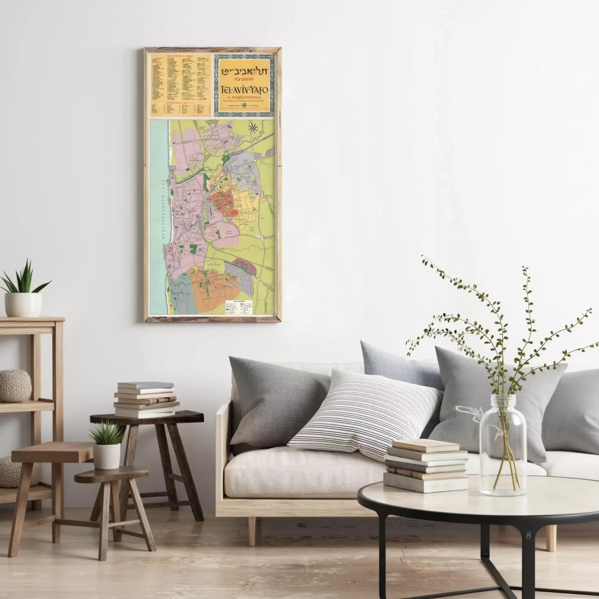 a living room with a large wall-mounted map of Tel Aviv, Israel, above a gray sofa with striped pillows. The room also includes a coffee table with books and a vase of greenery.