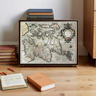 a framed map of the island of Iceland, with a stack of books and a book on a wooden floor in the foreground.