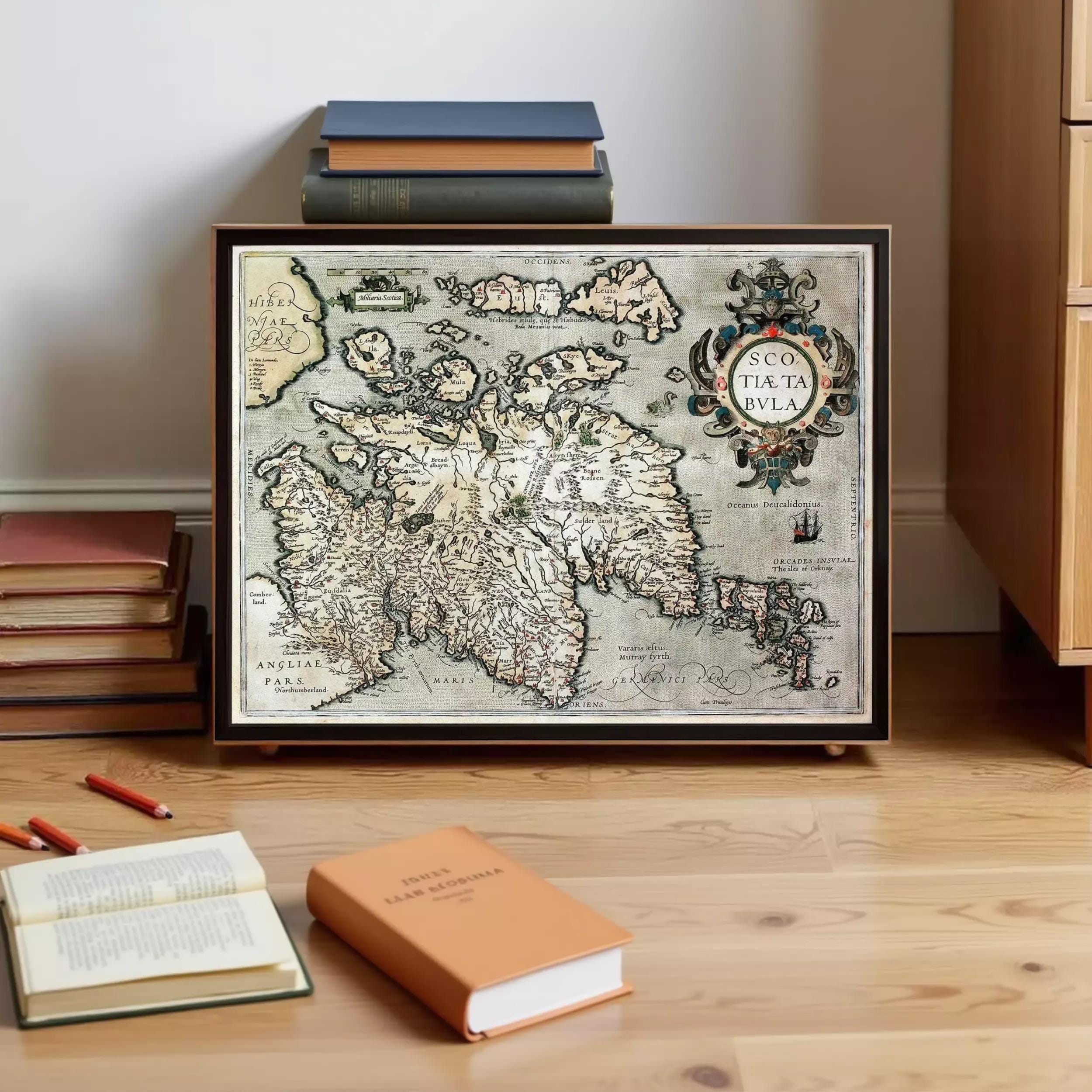 a framed map of the island of Iceland, with a stack of books and a book on a wooden floor in the foreground.