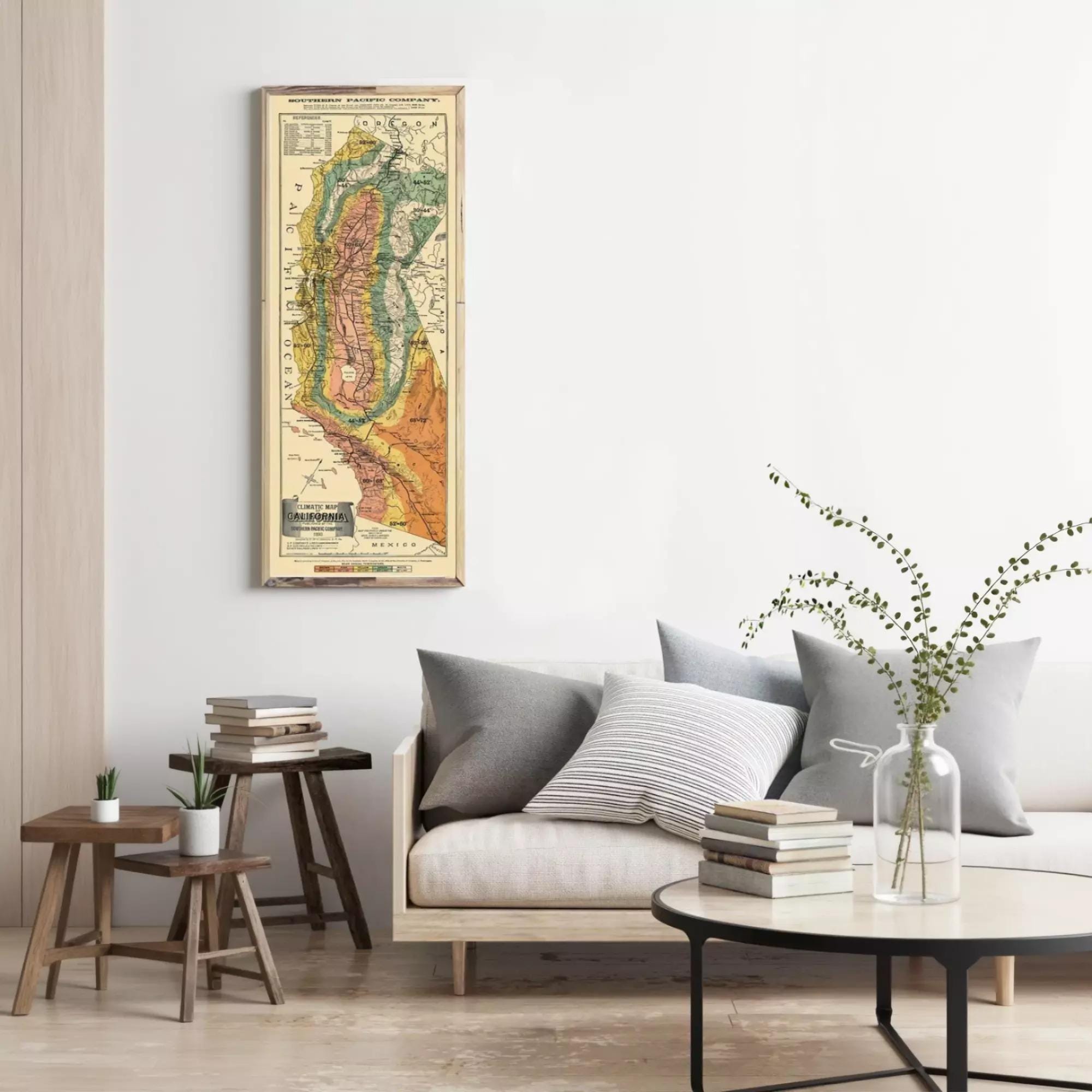 a living room with a large framed map hanging on the wall, a white sofa with gray and white striped pillows, a wooden side table, and a round coffee table with a vase of greenery.