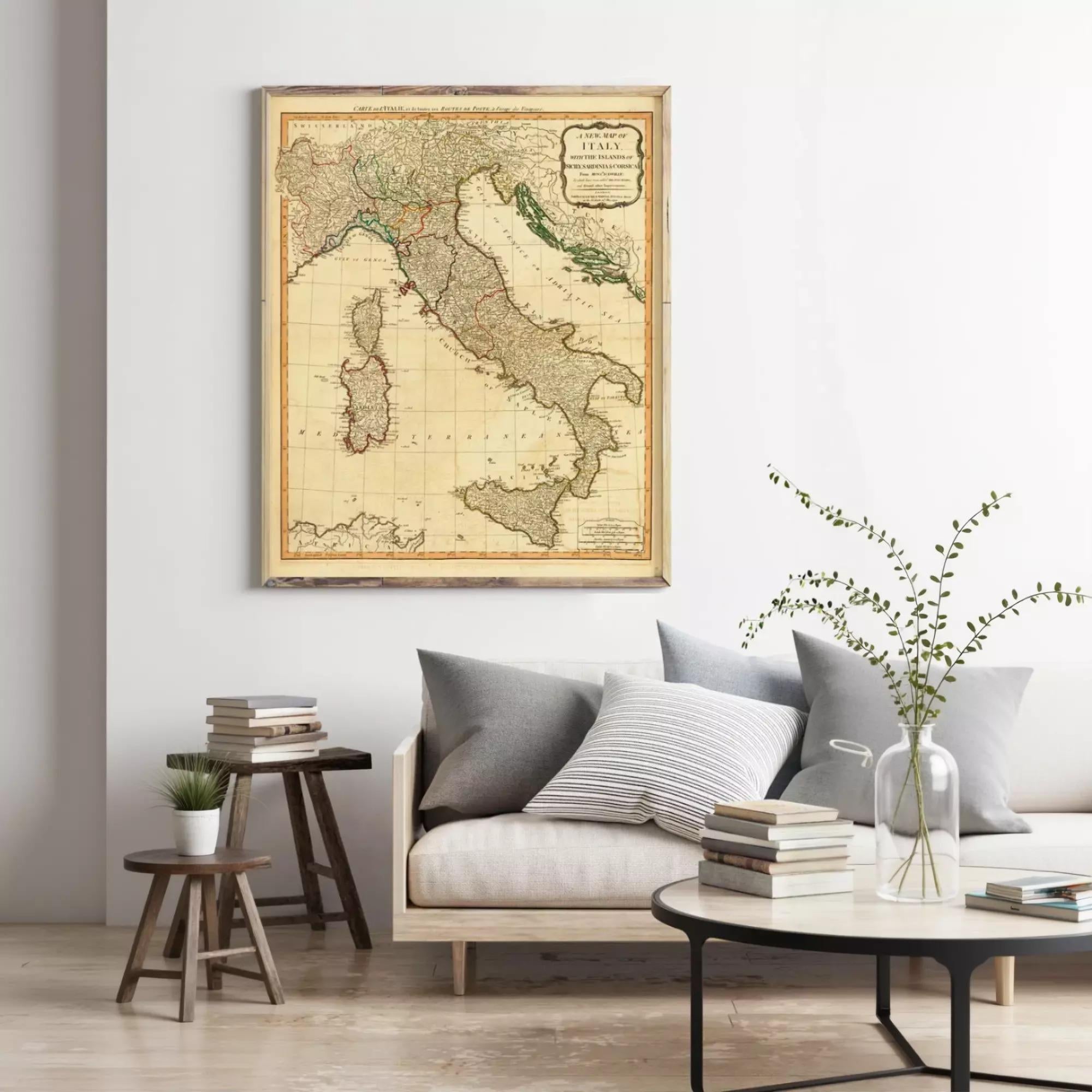 a living room with a large framed map of Italy hanging on the wall above a couch with pillows. There are also some books and a vase with greenery on the couch.