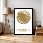A framed map of Sacramento, California, with the text "Sacramento" and "38°37'11" N, 28°28'11" W" below it, is displayed on a wall next to a lamp and a stack of books.