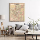 a living room with a large framed map of the city of Rockford, Illinois, hanging on the wall above a couch with pillows. There are also some books and a vase with greenery on the coffee table in front of the couch.