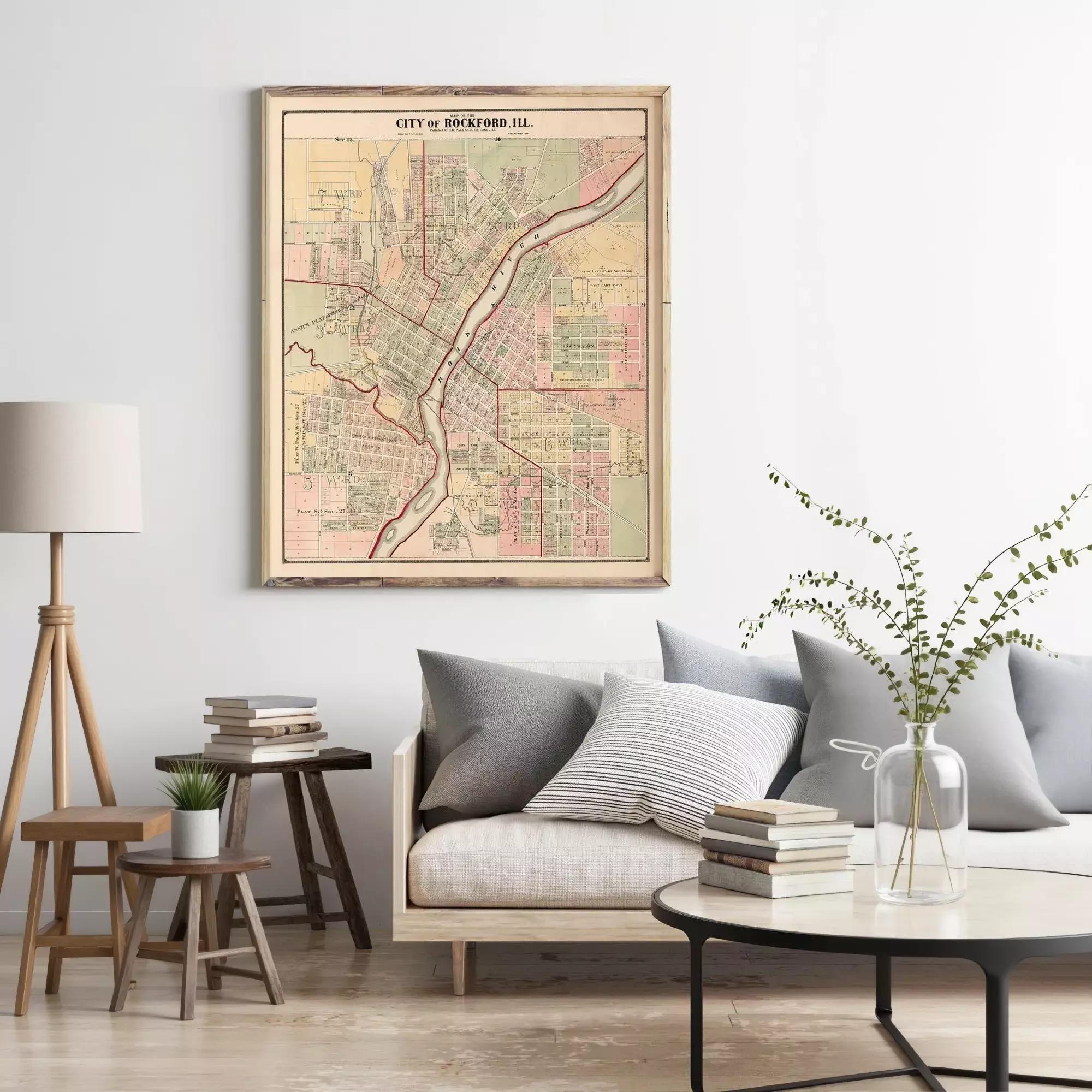 a living room with a large framed map of the city of Rockford, Illinois, hanging on the wall above a couch with pillows. There are also some books and a vase with greenery on the coffee table in front of the couch.