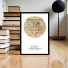 A framed map of Lyon, France, with a wooden floor and a stack of books in the background.
