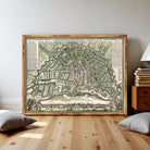 The image is a framed antique map of Amsterdam, featuring detailed illustrations of the city's streets, buildings, and waterways.