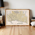 The image is a framed vintage map of a city, likely from the 19th century, displayed on a white wall.