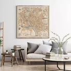 a living room with a large framed map of Budapest hanging on the wall above a couch with pillows. There are also some books and a vase with greenery on the couch, creating a cozy and inviting atmosphere.