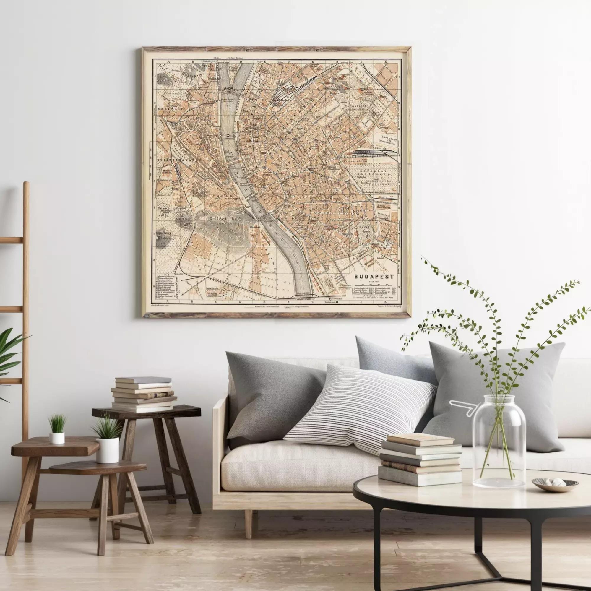 a living room with a large framed map of Budapest hanging on the wall above a couch with pillows. There are also some books and a vase with greenery on the couch, creating a cozy and inviting atmosphere.