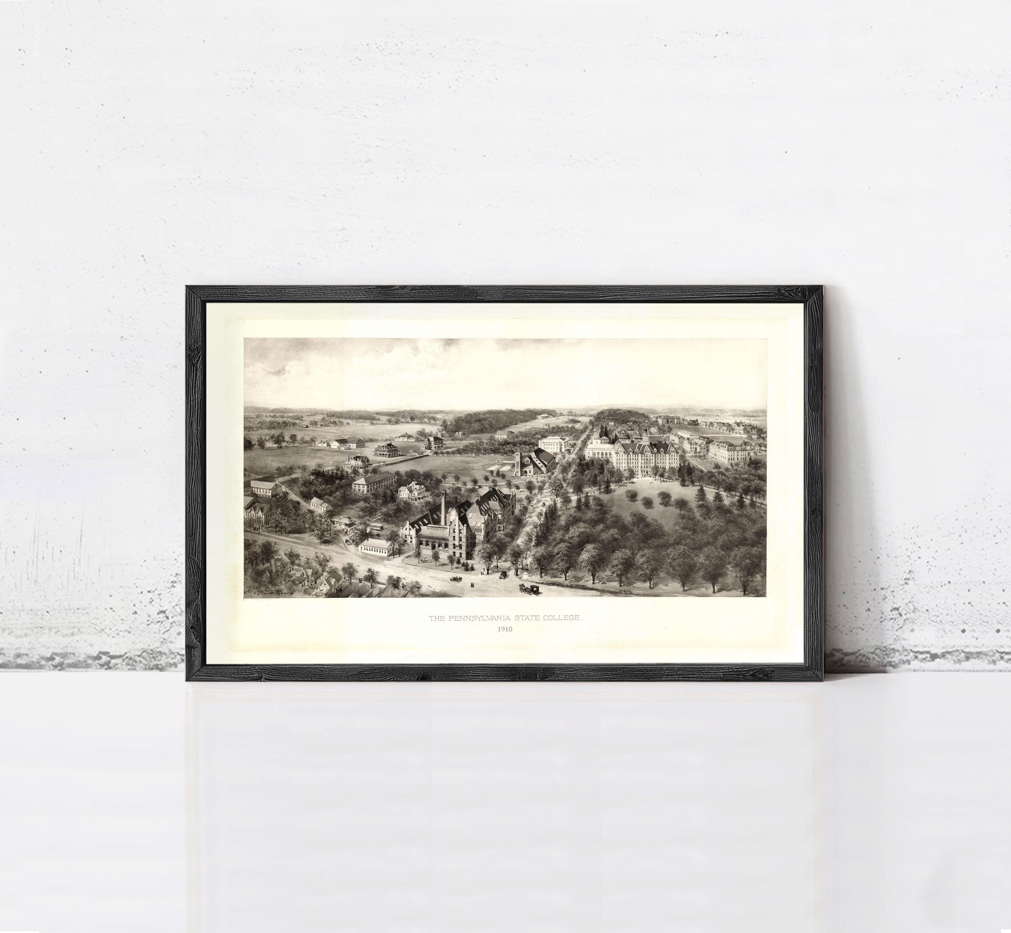 A framed black and white illustration depicting a rural landscape with buildings, trees, and a road.