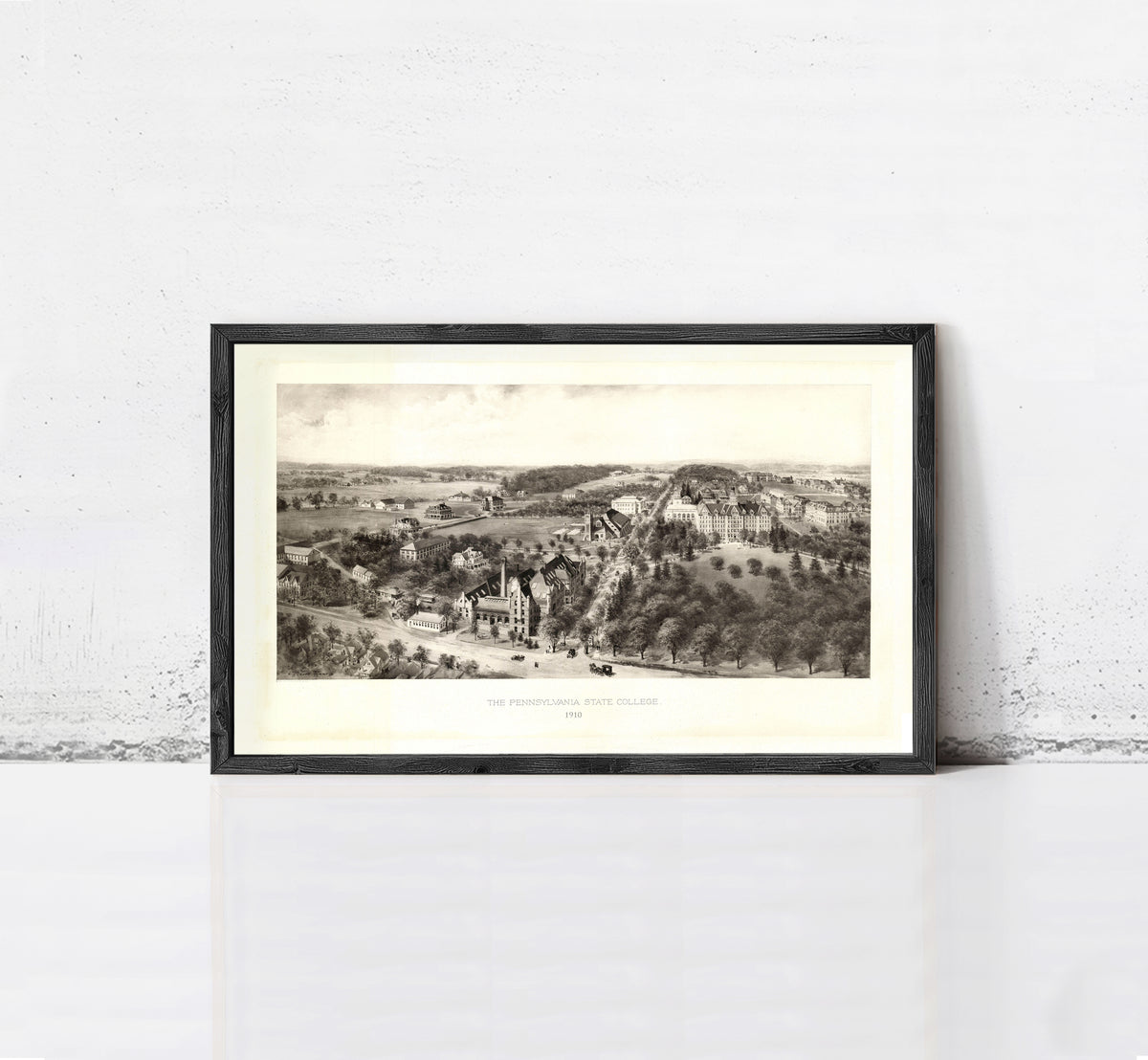 A framed black and white illustration depicting a rural landscape with buildings, trees, and a road.